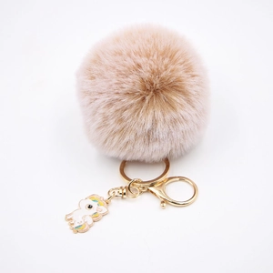 Détail d'un porte-clés pompon rose clair avec un charme licorne émaillé et un crochet doré