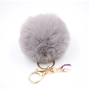 Detail of soft grey faux fur pompom keychain with golden clasp and unicorn charm