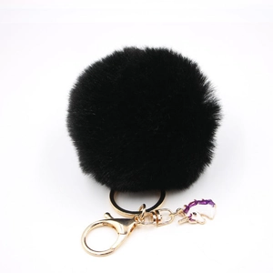 Detail of fluffy black faux fur pompom keychain with golden metal ring and unicorn charm