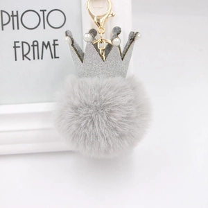 Détail d'un porte-clés pompon gris avec couronne à paillettes et fermoir en métal doré