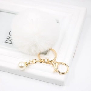 Detailed macro view of white faux fur pompom keychain with golden metal ring and pearl charm