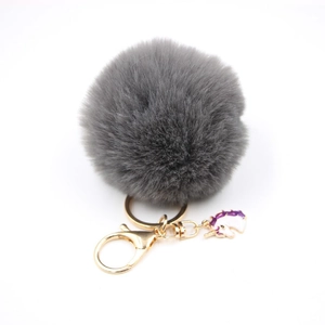 Detailed close-up of dark grey faux fur pom pom keychain with gold ring and purple unicorn charm