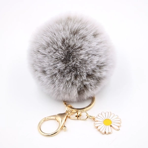 Détail d'un porte-clés pompon gris avec fermoir doré et pendentif fleur de marguerite blanche
