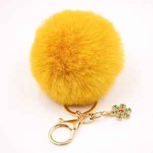 Détail d'un porte-clés pompon en fausse fourrure jaune avec flocon en émail vert et strass