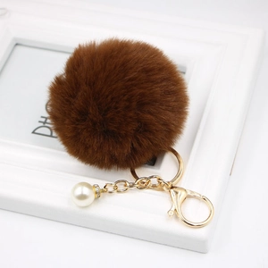 Detail view of coffee fur pompom keychain with golden clasp and elegant pearl accessory