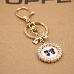 Detail of a golden bow keychain with white faux pearls and a black enamel S-letter pendant
