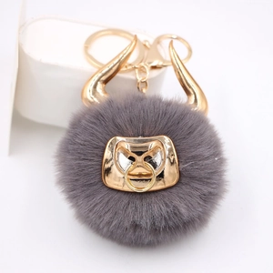 Detail of dark gray fluffy bull keychain with gold horns and metallic nose ring charm