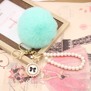 Detailed close-up of mint green faux fur pompom with pearl chain and vintage bow pendant