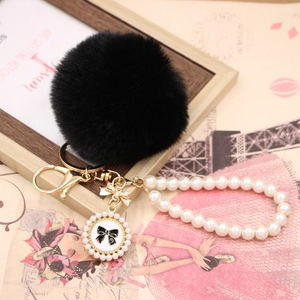 Detail of black faux fur pompom keychain with pearl chain and bow charm number five