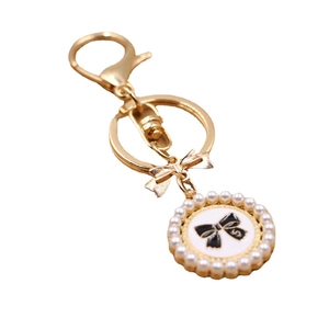 Golden keychain with pearl-beaded round pendant and black ribbon bow design charm