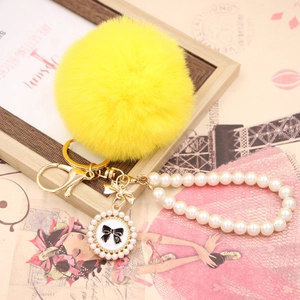 Detailed close-up of yellow faux rabbit fur pompom keychain with gold bow and pearl strap