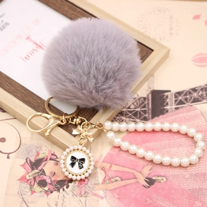 Close-up of a grey faux rabbit fur pompom with pearl chain and bow charm detail