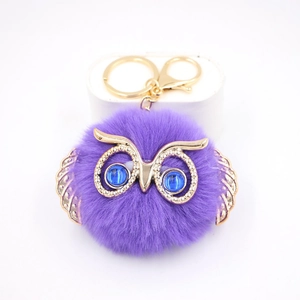 Détail du porte-clés pompon hibou violet avec ailes dorées et yeux bleus brillants