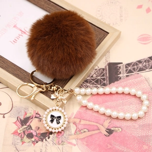 Detail of a brown faux rabbit fur keychain with pearl chain and golden bow charm