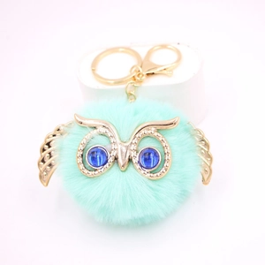 Détail du porte-clés pompon chouette bleu Tiffany avec des ailes dorées et des yeux en gemme