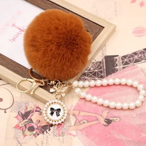 Close-up of brown faux fur ball keychain with pearl strap and gold bow detail