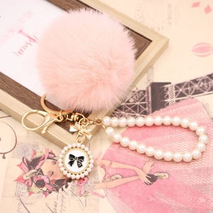 Detail of pink faux fur pompom with pearl bead chain and golden bow pendant keychain