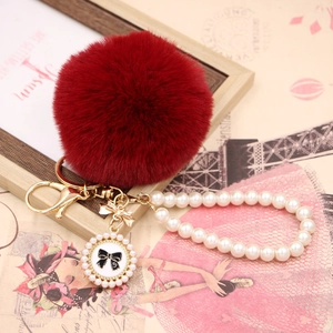 Detailed close-up of dark red faux fur pompom with golden bow and pearl chain strap