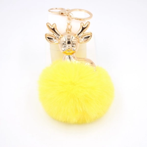 Détail de la breloque tête de cerf dorée avec un pompon en fausse fourrure jaune doux