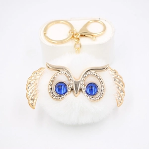 Détail d'un porte-clés hibou en peluche blanche avec finitions dorées et yeux bleus