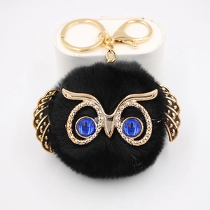 Gros plan du porte-clés hibou en pompon noir avec des ailes dorées et des yeux bleus
