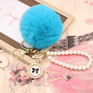 Detail of sky blue faux fur pompom keychain with pearl chain and number five charm