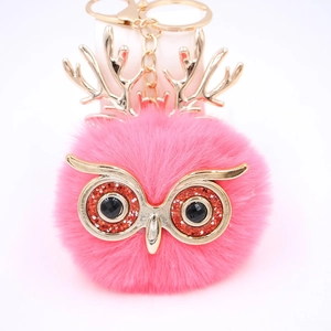 Gros plan du porte-clés hibou rose moelleux avec bois dorés et yeux scintillants