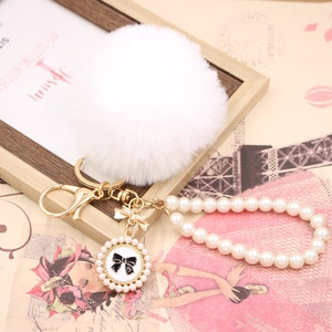 Detail showing white faux fur pompom with pearl wristband and golden bow charm
