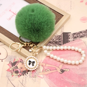 Detail of green faux fur pompom keychain with pearl wristlet strap and number five charm
