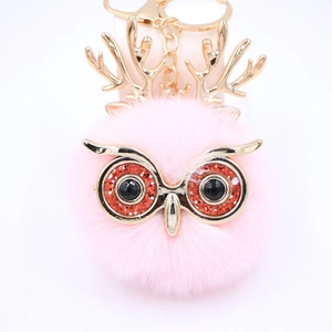 Détail d'un porte-clés hibou en peluche rose avec bois dorés et grands yeux pailletés