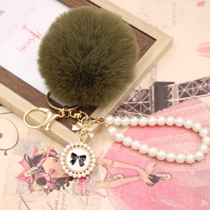 Close-up of olive green faux fur pompom with pearl bead chain and golden lobster clasp