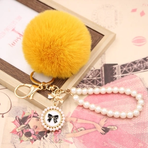 Close-up of yellow faux fur pompom keychain with pearl chain and bow detail on magazine