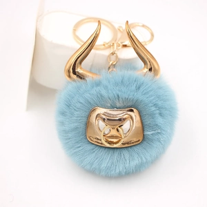 Macro detail of a light blue faux fur bull keychain with gold metal horns and nose ring
