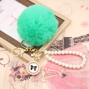 Detail of mint green faux rabbit fur pom pom with pearl chain and golden bow charm