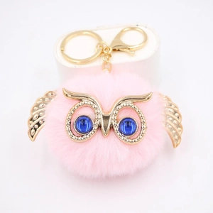 Détail d'un porte-clés hibou rose en fourrure avec ailes dorées et yeux bleus brillants