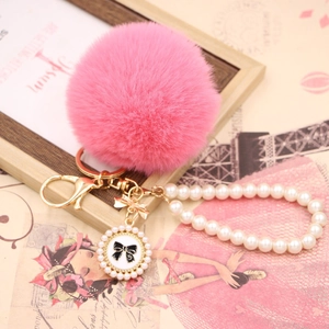 Close-up of pink faux rabbit fur pompom with pearl chain and bow pendant charm