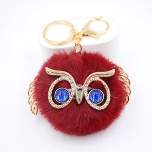 Détail d'un porte-clés hibou en peluche rouge avec des ailes dorées et des yeux bleus