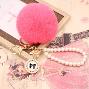 Close-up of bright pink faux fur pompom keychain with pearl strap and bow pendant