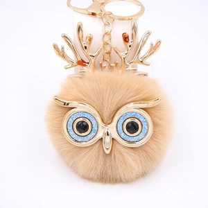 Détail d'un porte-clés chouette en peluche avec bois dorés et yeux à paillettes bleues
