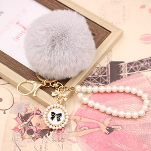 Detail of grey faux fur pompom keychain with pearl chain and bow charm on a retro background