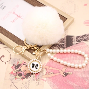 Close-up of a white faux fur ball keychain with pearl strap and bow pendant detail