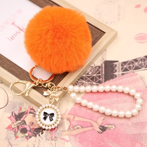 Close-up of bright orange faux fur pompom keychain with pearl strap and bow charm