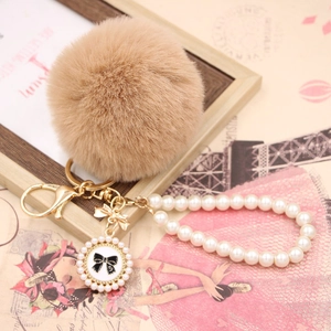Detail of khaki faux rabbit fur pom pom with pearl strap and bow pendant on gold chain