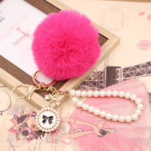 Detailed view of rose pink faux fur pompom keychain with pearl strap and gold bow charm