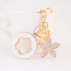 Gold-tone keychain featuring white enamel flower and sparkling rhinestone lucky clover charm