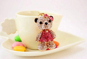 Close-up of crystal bear keychain featuring pink rhinestone dress on golden alloy finish