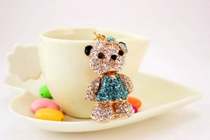 Detailed view of crystal teddy bear charm with blue rhinestone dress on a ceramic cup