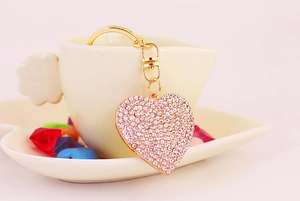 Detailed macro view of heart-shaped rhinestone keychain hanging on a white coffee cup