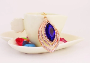 Detailed close-up of peacock feather pendant with blue gemstone and rose gold finish