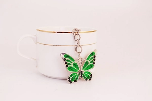 Dettaglio di un portachiavi a farfalla in smalto verde appeso a una tazza di ceramica
